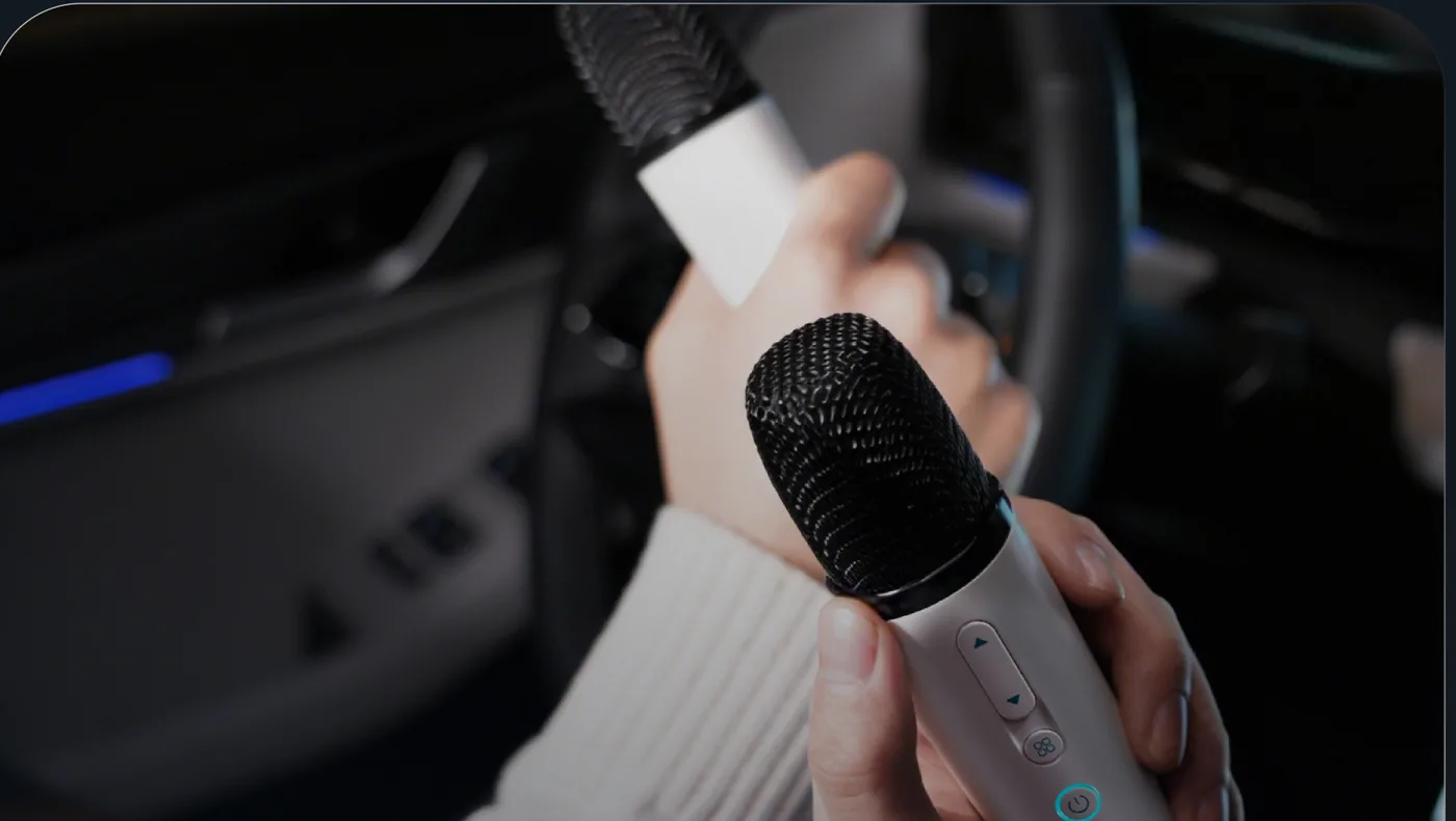 A hand holding the J5 EV wireless karaoke microphone at the steering wheel.